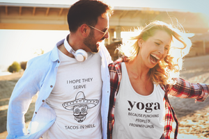 A man and a woman on a beach are wearing Fun t-shirts saying - I hope they serve tacos in hell and yoga-because punching people is frowned upon. 